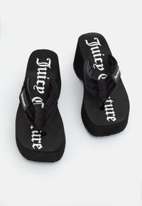 Black flip-flops with a textured black strap and white "Juicy Couture" branding on the footbed. Features a thick, cushioned sole.