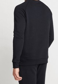 Svart sweatshirt, bomullsblandning, har raglanärmar, ribbade ärmslut och fåll. Slät struktur, minimalistisk design, inga synliga logotyper eller mönster.