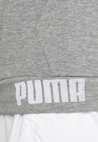 Tela de sudadera gris con dobladillo ribeteado en la parte inferior, que presenta un logotipo estilizado en blanco de "PUMA". Textura suave, diseño minimalista y estilo casual.