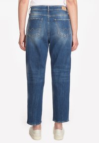 Vaqueros de mezclilla azul claro con un corte relajado, que presentan dos bolsillos traseros con un diseño de costura distintivo. Llevados con zapatos slip-on blancos.