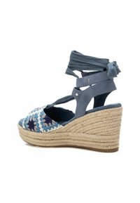 Sandal de cuña trenzada azul que presenta un tacón de yute tejido, correas ajustables en el tobillo y un área de los dedos decorada con un patrón en tonos azul y marino.