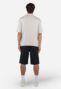Camisa de manga curta cinza-claro com um corte descontraído, combinada com calções pretos até ao joelho. O vestuário apresenta um design simples, sem padrões visíveis.