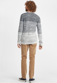 Grau-weißer Verlauf Strickpullover mit strukturierter Oberfläche, langen Ärmeln und rundem Halsausschnitt, kombiniert mit beigefarbenen Cordhosen.