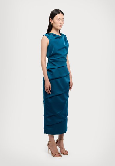 Satin kjole i teal med rund udskæring, lagdelt drapering og tætsiddende silhuet, parret med nude ankelremssandaler.