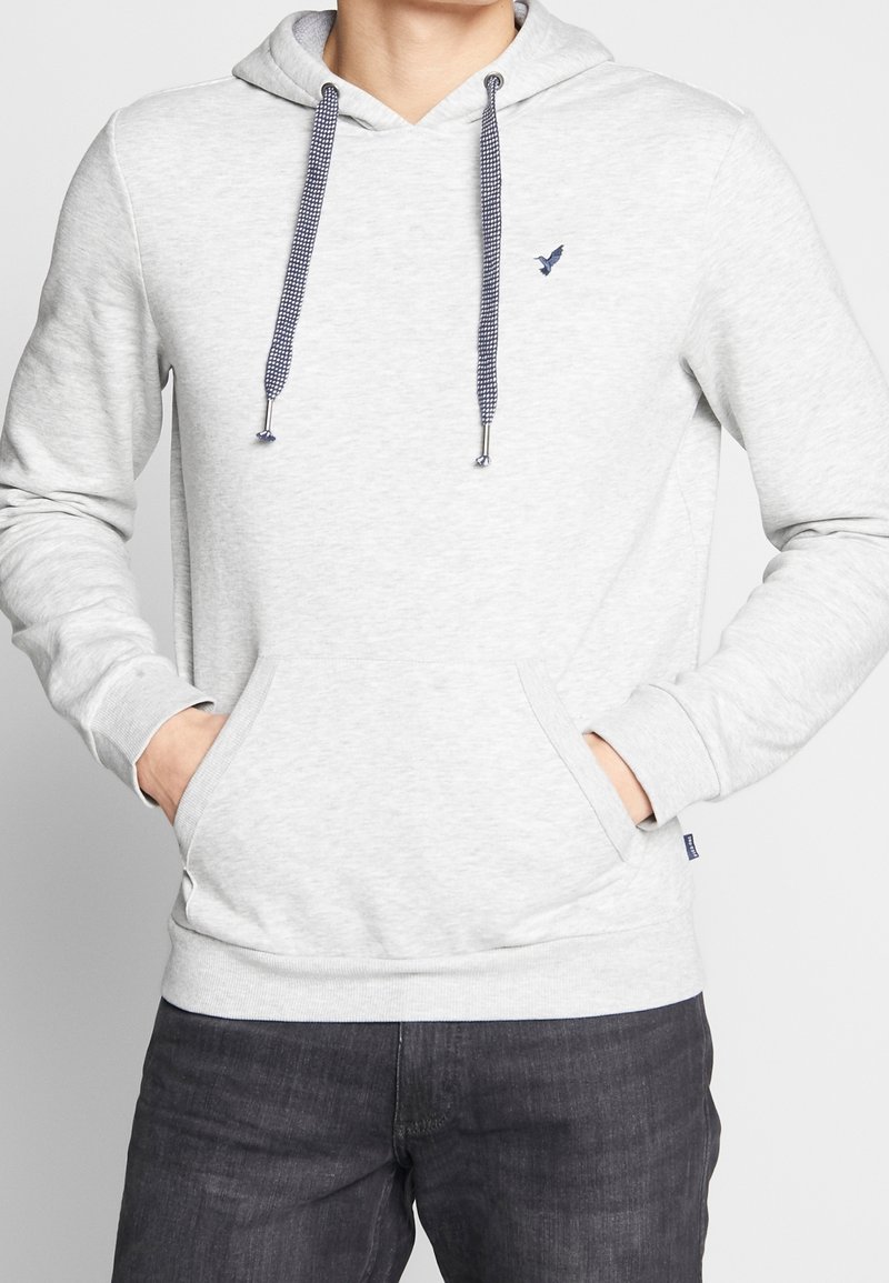 Grå hoodie i mjukt tyg, med en framficka, justerbar huva med mönstrade dragsnören och en liten broderad logotyp på bröstet.