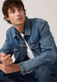 Τζιν μπουφάν με ανοιχτό μπλε ξέβαμμα, κλασικό γιακά, κουμπιά στο μπροστινό μέρος και δύο τσέπες στο στήθος. Λευκή μπλούζα Τ από κάτω.