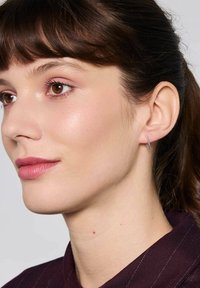 Srebrna kolczyk w kształcie obręczy przymocowany do ucha modelki; kolczyk ma wypolerowane wykończenie i smukły, krzywiznisty design.