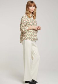 Blouse à motif avec un design en goutte d'eau vert et rose, associée à un pantalon large blanc. Le mannequin porte des bottes à talons noires.