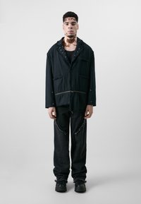 Schwarze, oversized Jacke mit fransigen Kanten, zwei Taschen und Knopfverschluss. Kombiniert mit ausgefransten schwarzen Hosen und klobigen schwarzen Stiefeln.