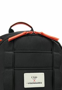 Zaino in nylon nero con design imbottito, cerniere arancioni a contrasto e un'etichetta bianca con testo nero. Include due manici superiori.