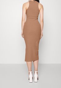 Abito midi aderente e a costine in un caldo tono di marrone, con scollatura alta e uno spacco moderato sul retro, abbinato a sandali bianchi con tacco a blocco.