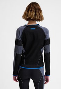 Zwarte sporttop met lange mouwen, grijze accenten en blauwe highlights. Heeft een getailleerd ontwerp met textuurpanelen en geribbelde details.