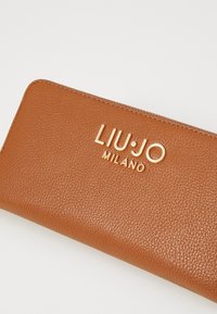 Portafoglio in pelle marrone con superficie testurizzata, caratterizzato da un logo dorato "LIU•JO MILANO" in evidenza sulla parte frontale.