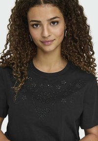 Camiseta de algodón negra con detalles de corte en forma de flor, mangas cortas y cuello redondo. Textura suave con acentos de diseño intrincados.