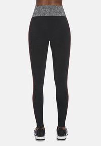 Czarne legginsy z szarym pasem w talii, z czerwonymi paskami po bokach. Materiał ma gładką fakturę, zaprojektowany do odzieży sportowej lub aktywnej.
