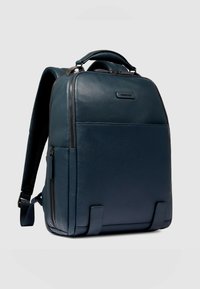 Zaino in pelle blu scuro con superficie strutturata, dotato di maniglia superiore, spallacci imbottiti e molteplici scomparti con cerniera.