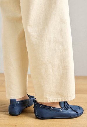 Blå läderskor med en slät yta, snörningsdetaljer och silverfärgade ögla, kombinerade med krämfärgade, löst sittande byxor.