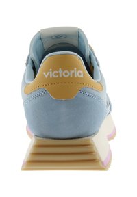 Achteraanzicht van een lichtblauwe sneaker met een beige hielpaneel met het label "victoria" en een beige zool met roze accenten.