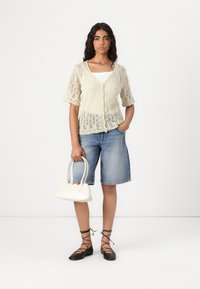 Light green knitted cardigan with short sleeves, paired with denim shorts. Accessories include a small white handbag and black lace-up flats.