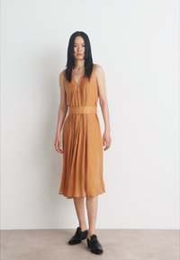 Robe midi plissée amber avec un décolleté en V profond et une ceinture assortie ; elle présente une texture douce et un design en couches avec une silhouette évasée.