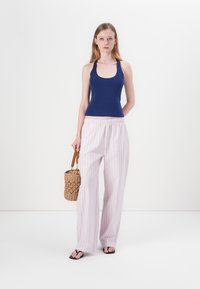 Námornícky tank top, svetloružové prúžkované široké nohavice, tkaná kabelka a čierne sandále. Hladká tkanina, voľný strih a uvoľnený dizajn.