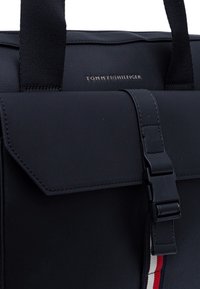 Borsa nera sintetica dal design strutturato, con chiusura a scatto, dettagli in tessuto a contrasto e logo impresso sulla parte anteriore.