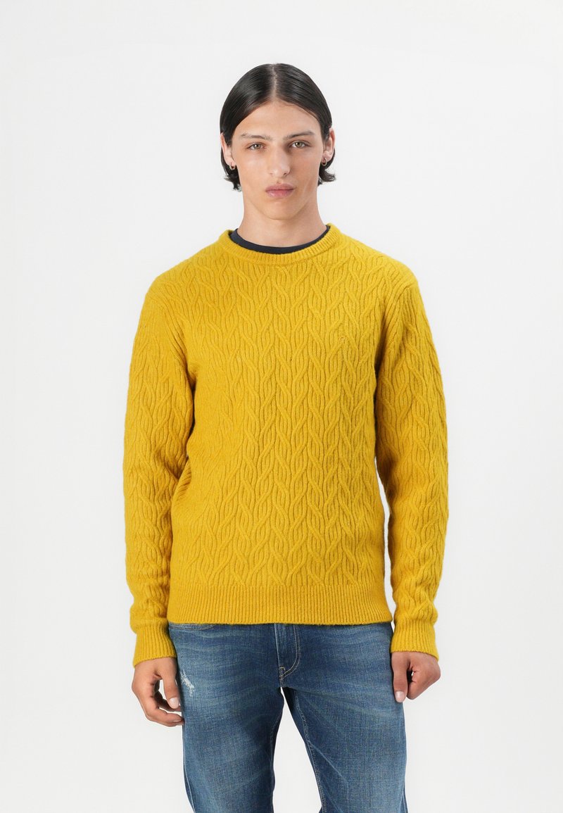 Pullover a maglia in un vivace giallo in lana, con un collo a girocollo a coste e maniche lunghe. Abbinato a jeans blu, per un look casual.