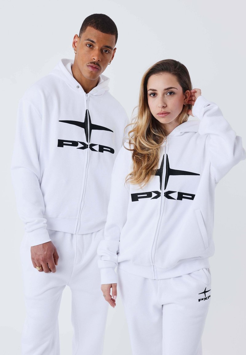 Sudaderas con cremallera blanca y pantalones de chándal a juego con logotipos negros. El tejido parece suave. Cuenta con bolsillos frontales y puños acanalados.