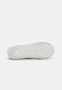 Sola di sneaker bianca con grip in gomma testurizzata, caratterizzata da motivi zigzag e circolari per una migliore aderenza. Bordo superiore liscio con curve delicate.