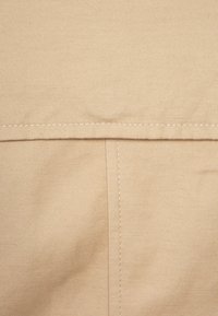 Beige stof met een gladde textuur, met een rechte naad langs de bovenkant en een verticale steek in het midden.