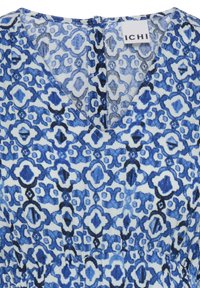 Blau-weiß gemusterte V-Ausschnitt-Bluse mit geometrischen Formen und eingenähtem "ICHI" Markenetikett am Ausschnitt.