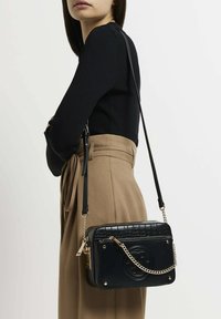 Svart crossbody-väska med krokodilmönstrad textur och detaljer i guld. Har en avtagbar kedjerem och logotypdetalj på framsidan.