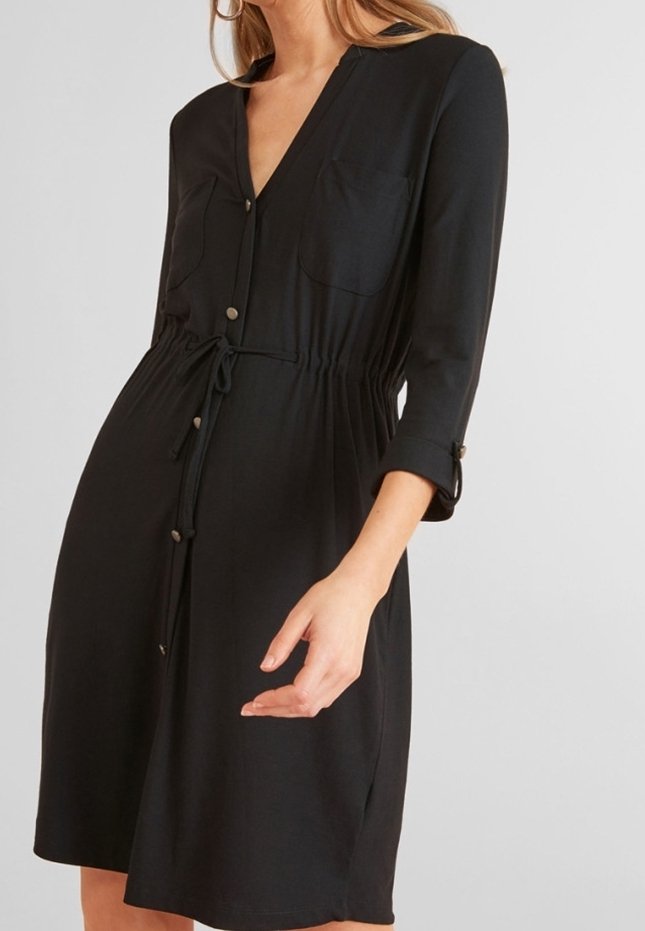 Robe noire mi-longue avec fermeture à boutons devant, taille avec cordon, poches poitrine et manches trois-quarts sur une personne devant un fond uni.