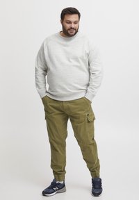 Sudadera de un gris claro con puños de canalé, combinada con pantalones cargo de color verde oliva que tienen bolsillos laterales. Unos zapatos deportivos en negro y gris completan el conjunto.