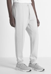 Pantalons de jogging tapered gris clair en tissu doux, dotés de poches avant, d'une taille à cordon de serrage et de coutures subtiles, associés à des baskets grises.
