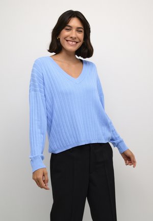 Lichtblauwe geribbelde trui met een V-hals en lange mouwen; textuurstof met een relaxed fit, gecombineerd met zwarte broek.