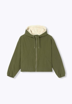 Veste courte vert olive avec fermeture éclair frontale, deux poches, poignets élastiques et capuche doublée de polaire crème.