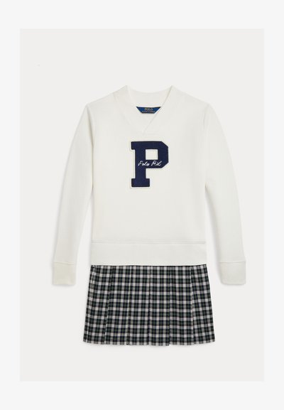 Κρέμα πουλόβερ με λογότυπο "P" σε ναυτικό και κεντημένο "Polo RL", συνδυασμένο με πλισέ καρό φούστα σε σκούρο πράσινο, ναυτικό και λευκό.