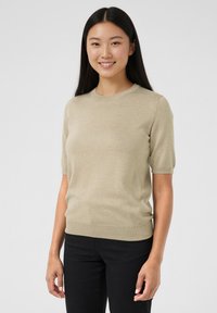 Beige striktrøje med korte ærmer, rund hals, blød tekstur og ribbet kant, kombineret med sorte bukser.