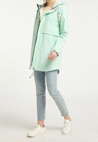 Veste imperméable vert menthe avec fermeture éclair à l'avant, capuche et cordons de serrage ajustables. Présentée avec des manches longues et deux poches avant.