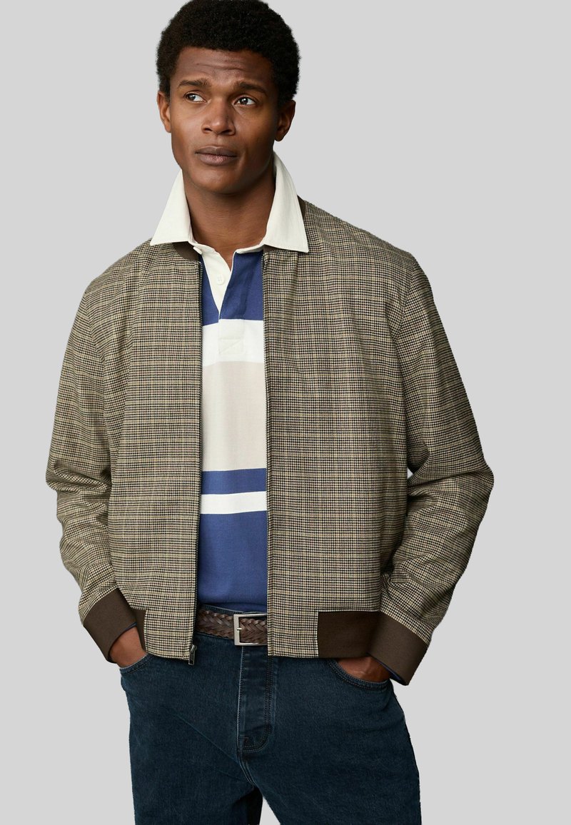 Checkered brown bomber jacket with a ribbed dark brown hem, layered over a blue and white striped polo shirt, with a textured finish.