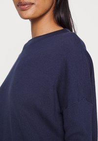 Pull en maille bleu marine avec encolure ronde et épaules légèrement tombantes ; texture lisse avec une coupe regular.