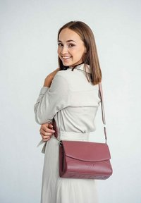 Středně růžová kožená taška přes rameno s designem klapky, embosované logo na přední straně a odnímatelný popruh. Hladký povrch s minimálním kováním.