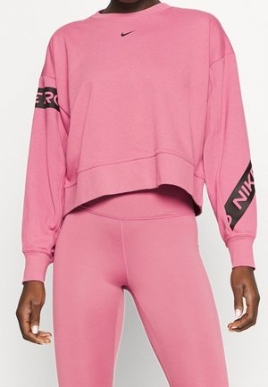 Personne portant un sweat court rose Nike avec logo sur la poitrine et les manches, assorti à un legging rose.
