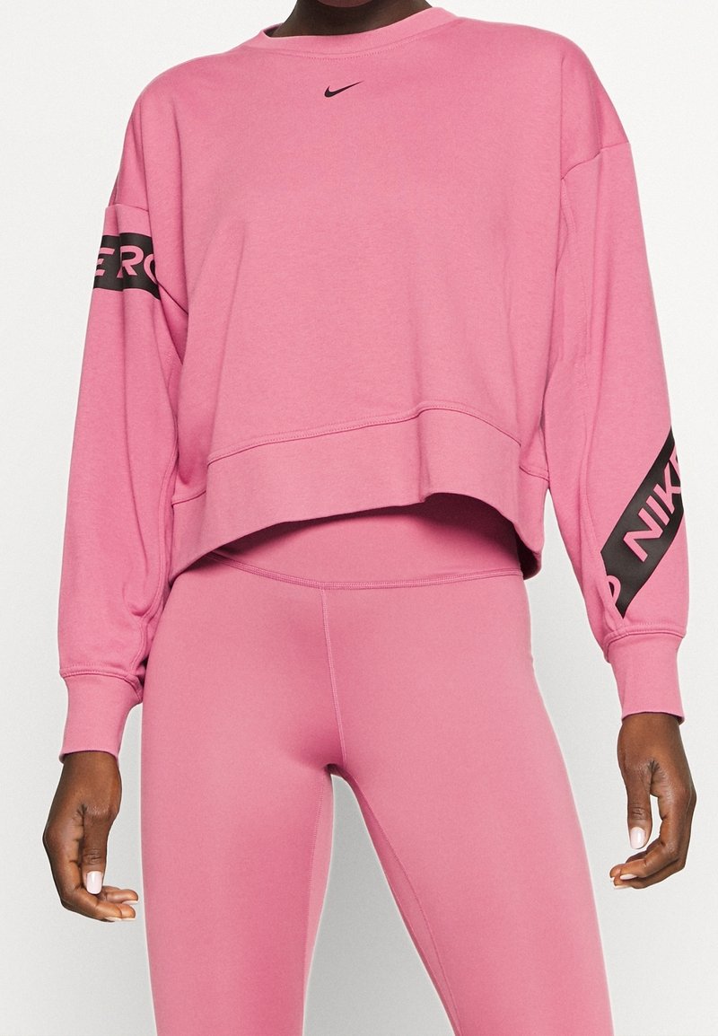 Personne portant un sweat court rose Nike avec logo sur la poitrine et les manches, assorti à un legging rose.