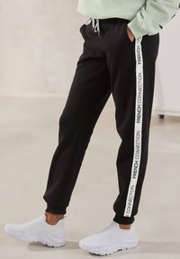 Schwarze Jogginghosen mit weißen Seitenstreifen und dem Schriftzug "FRENCH CONNECTION". Hergestellt aus weichem Stoff, taillierter Schnitt mit elastischen Bündchen.