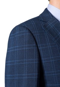 Granatowa w kratę marynarka z teksturowanej tkaniny, charakteryzująca się wyraźnie zarysowanymi ramionami i niebieskimi akcentami kraty. Zbliżenie na szew ramienia.