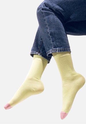 Żółte skarpetki o jednolitej fakturze, z różowym akcentem na palcach. Noszone z podwiniętymi dżinsami, co nadaje casualowy styl.