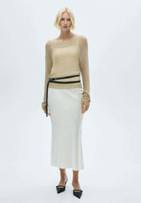 Pulover din tricot, subțire, de culoare aurie, asociat cu o fustă din satin albă, lungă până la podea, strânsă în talie cu o curea neagră. Pantofi de balerină negri, cu vârful ascuțit.