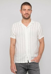Chemise à manches courtes avec col en tissu blanc à rayures verticales noires. Elle possède une fermeture à boutons et un tissage texturé.